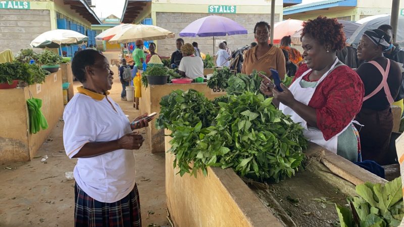 Two women engaging in a transaction and holding mobile phones at a market