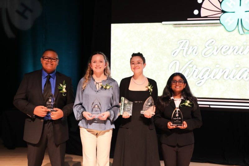 Four teens stand on a dark stage, holding awards.