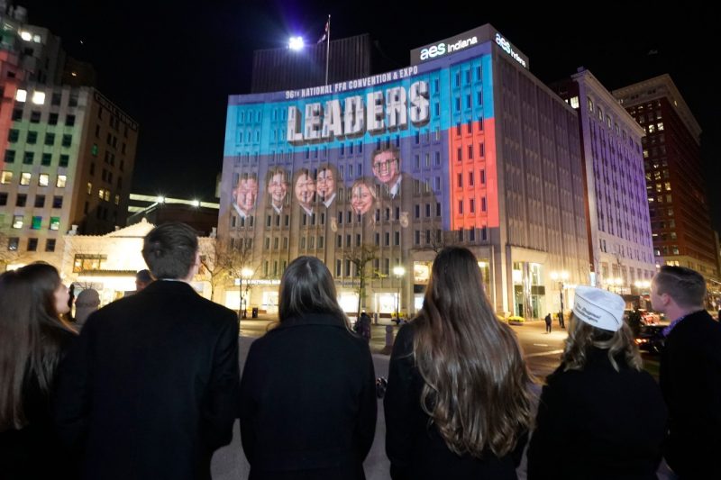 A downtown building lit up at night with a giant FFA photo.