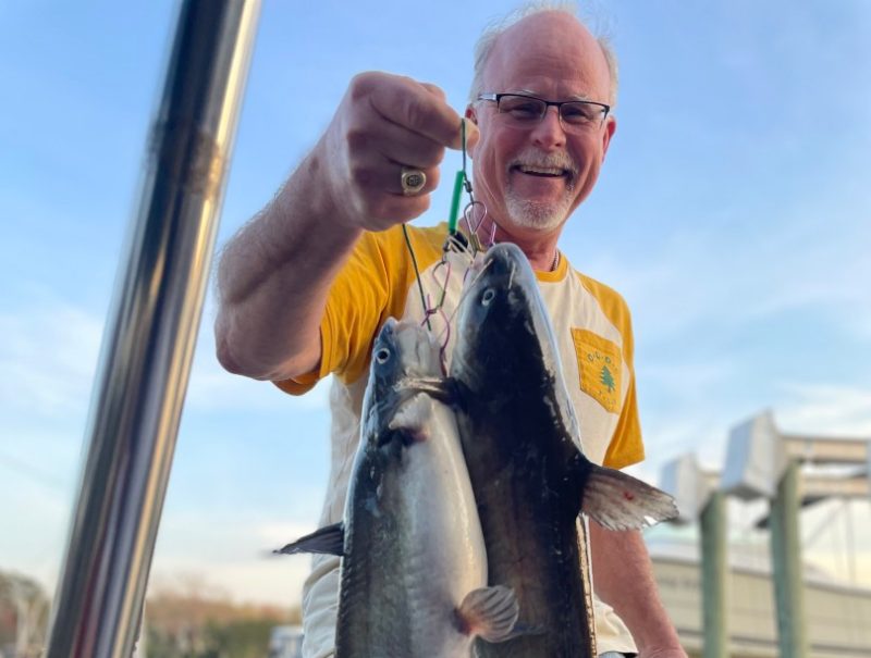 A man holds a fish stringer with two blue catfish