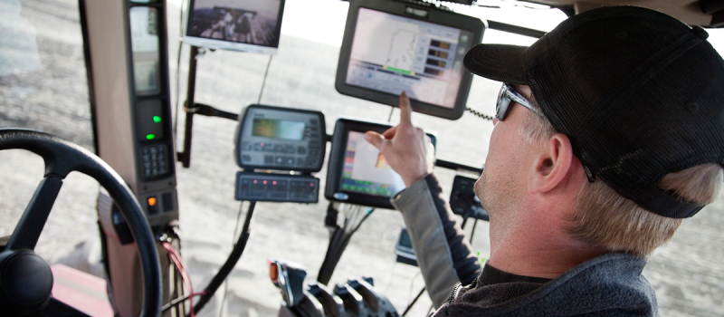 Image of a man in farm equipment pointing to screens in front of the passenger window.