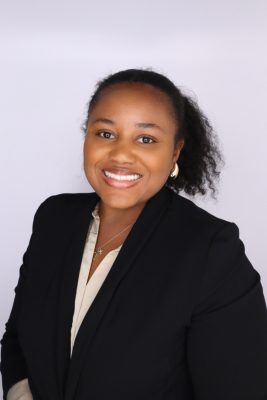 Black woman with natural hair wearing a dark suit and light shirt. 