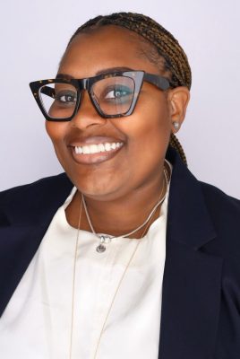 Black woman with braids pulled back wearing a white shirt and black blazer with glasses, smiling