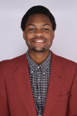Black man in red suit, smiling, standing in front of white background