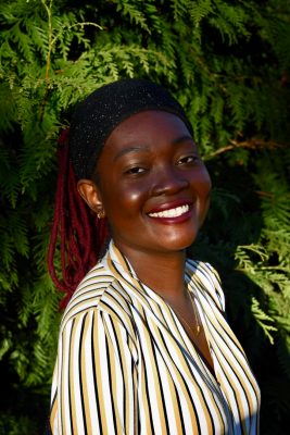 Black woman smiling in the sun standing in front of greenery