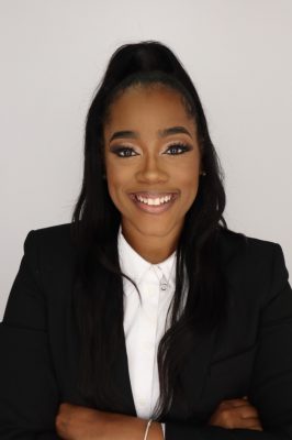 Black woman smiling, wearing a black suit over a white shirt, arms crossed over her chest